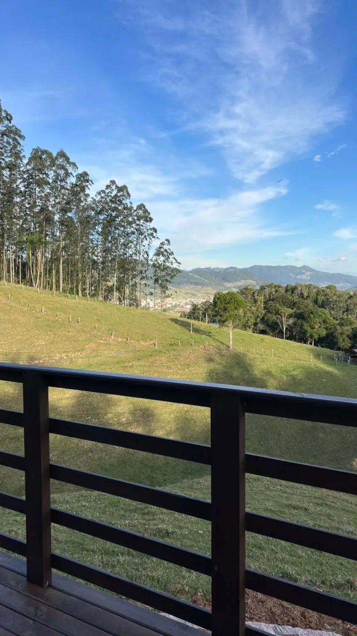 Deck de madeira com guarda-corpo e o vale verde com eucaliptos e a serra ao fundo