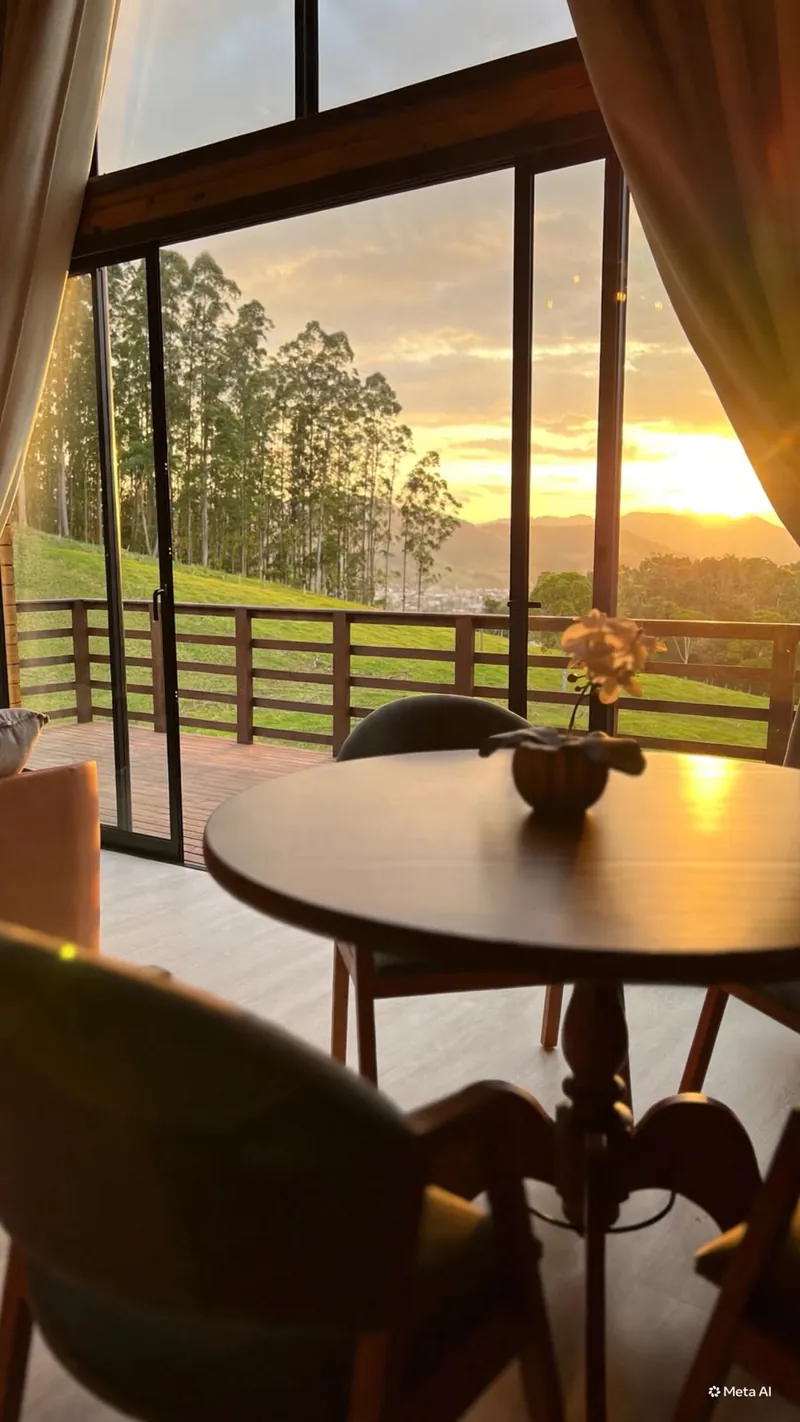 Mesa redonda junto ao vidro com o pôr do sol e os eucaliptos ao fundo